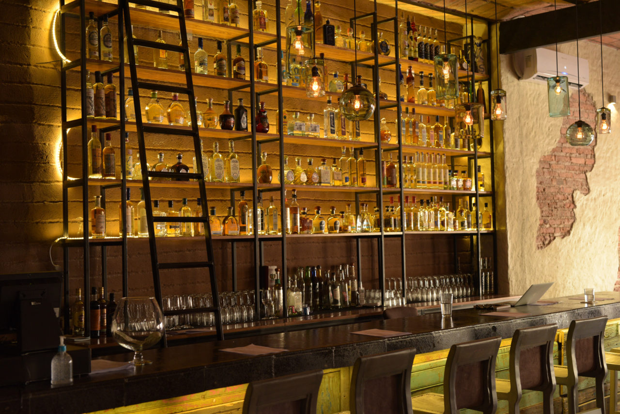 Bar area with shelves of alcohol behind bar. 