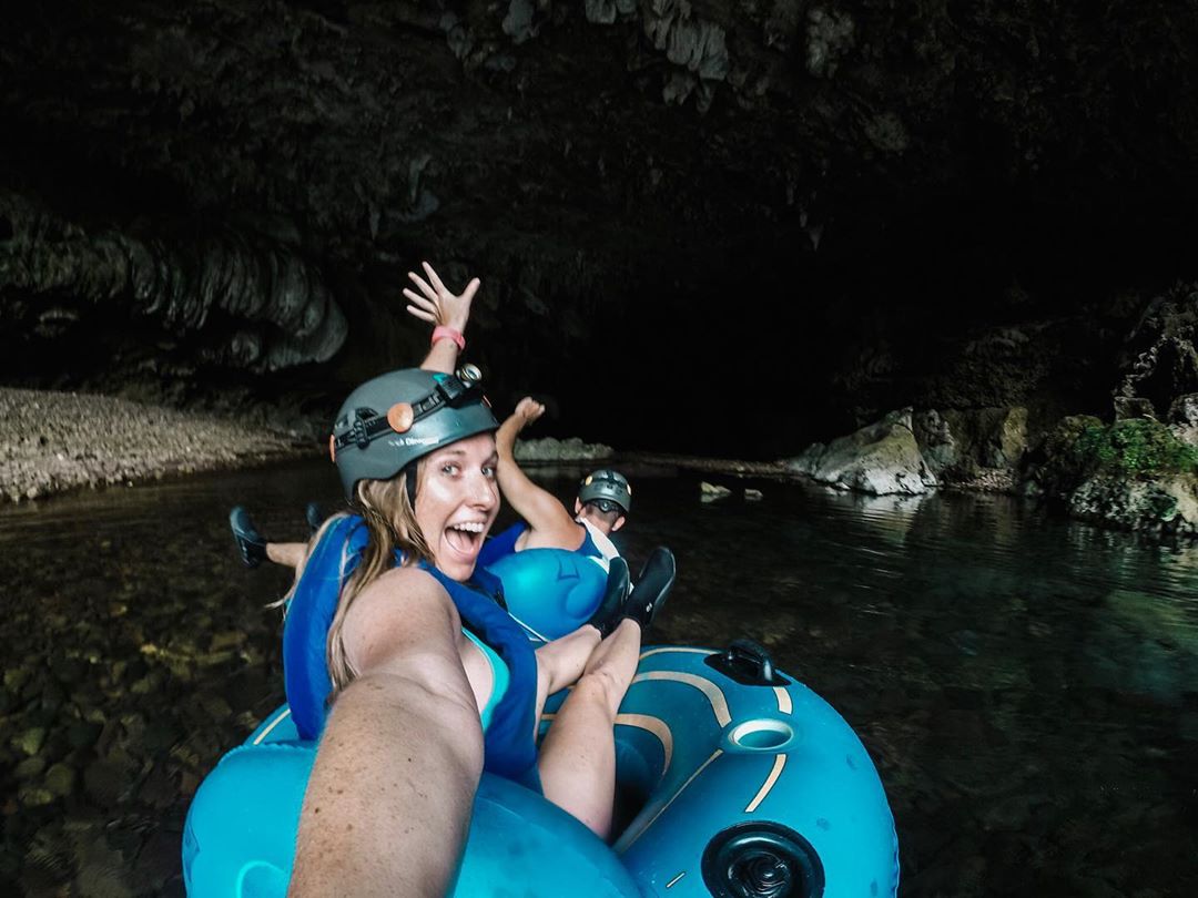 Girl holding camera while tubing through underground cave.