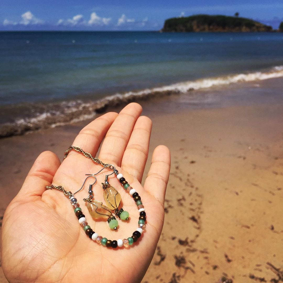 Person holding earrings and a necklace in their hand by the ocean. 