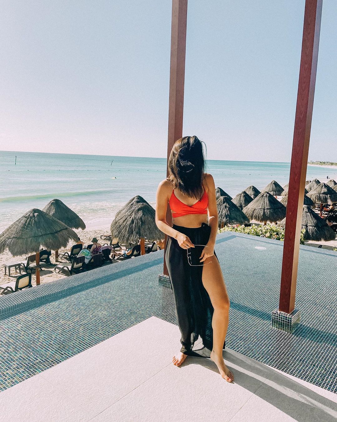 Girl standing by infinity pool by beach.