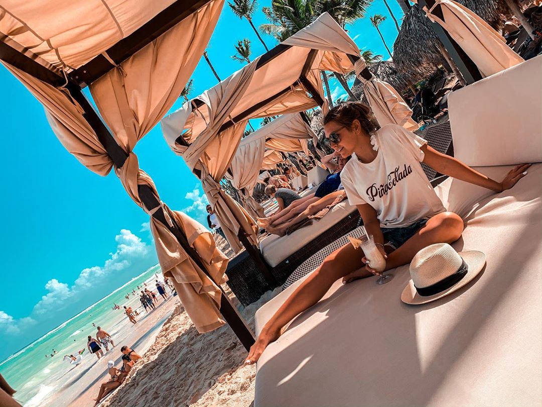 Girl sitting on beach Bali bed with piña colada.